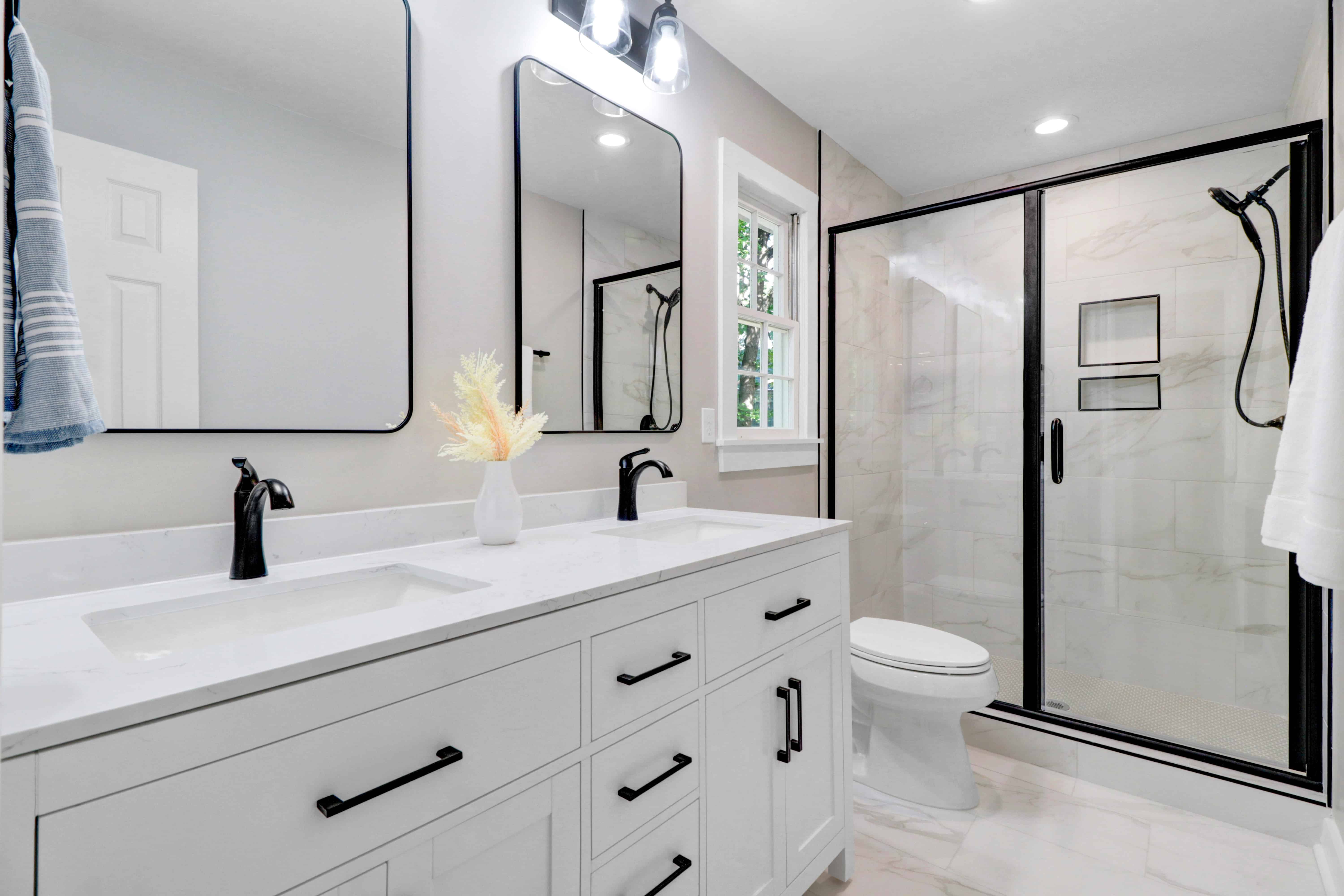 Renovated bathroom with a white double vanity, black fixtures and a marble-tiled glass shower
