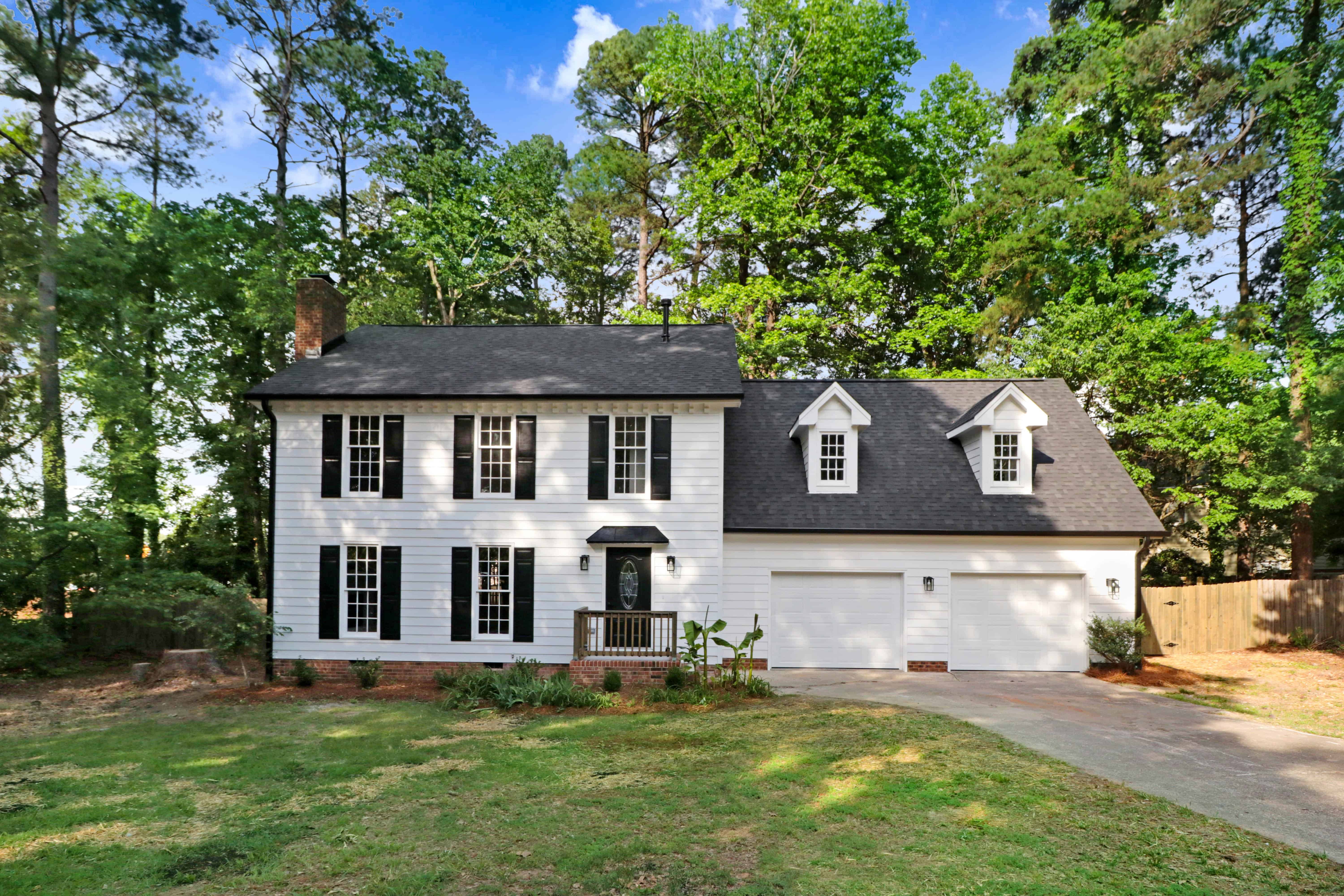 Exterior of a renovated two-storey Durham home with white siding, black shutters and a double garage