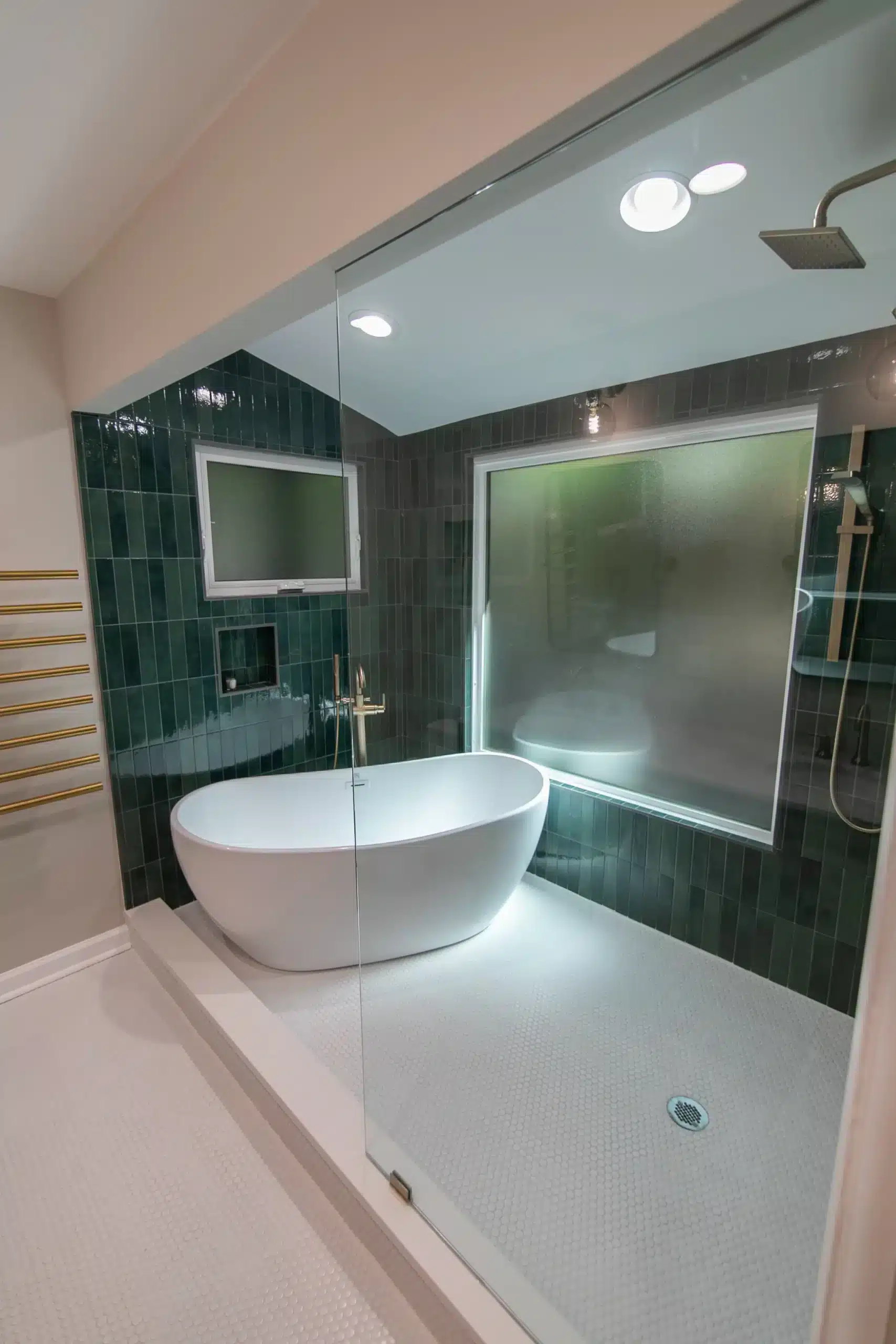 Wet room with dark green vertical tile, a freestanding tub and a rain shower behind a glass screen