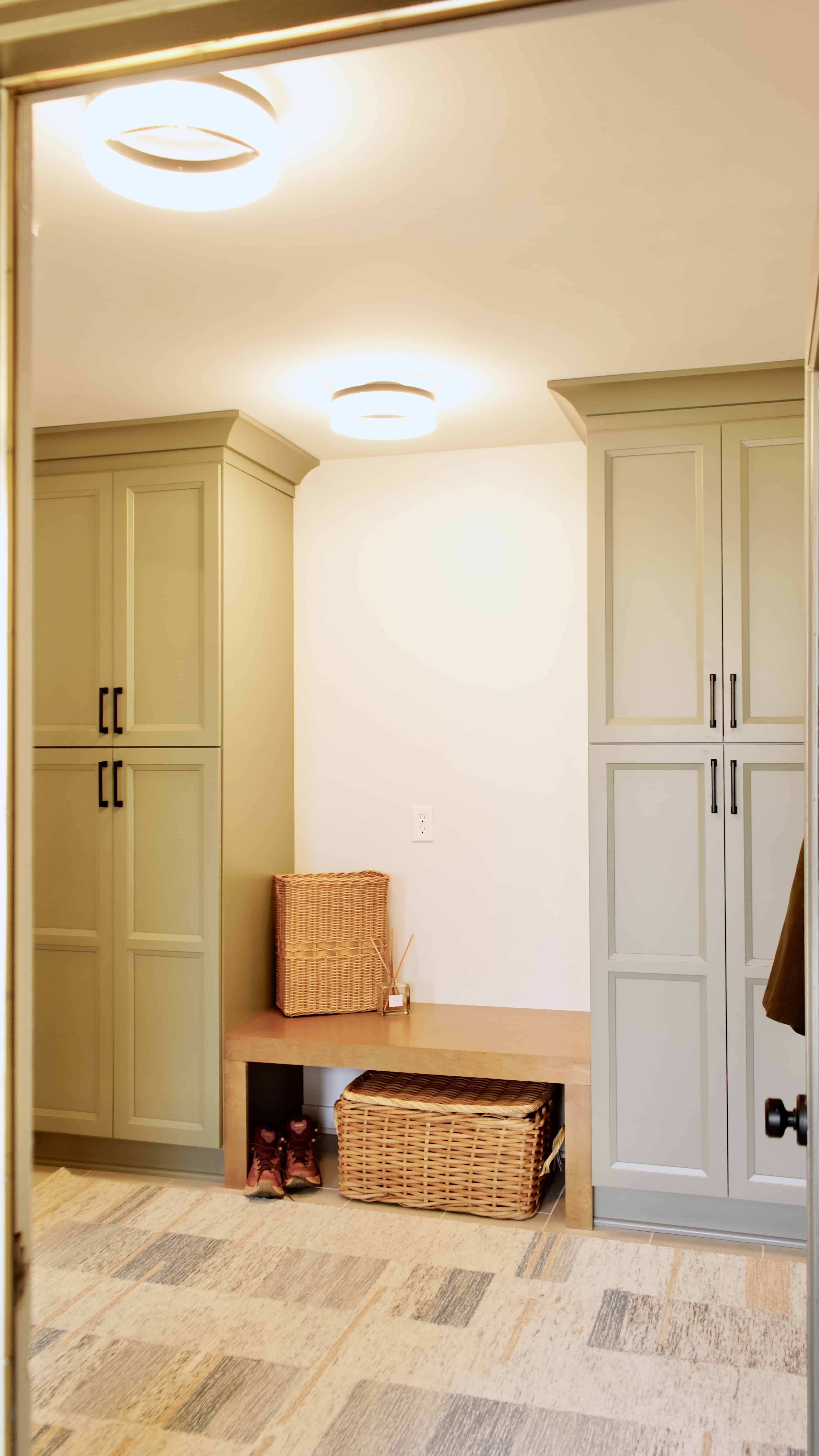 Mudroom with sage green floor-to-ceiling built-in cabinetry, a timber bench and storage baskets