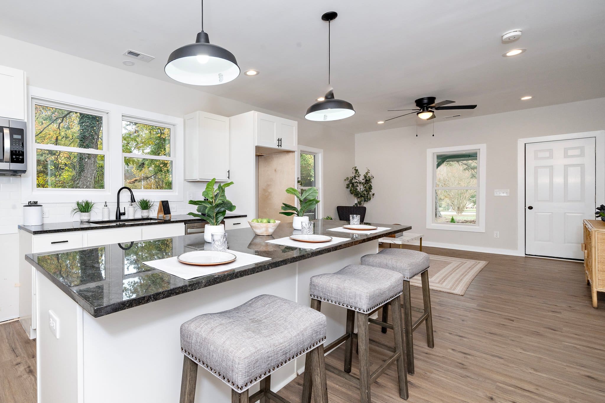 Open-plan kitchen with a granite breakfast bar, white cabinetry, bar stools and black pendant lights