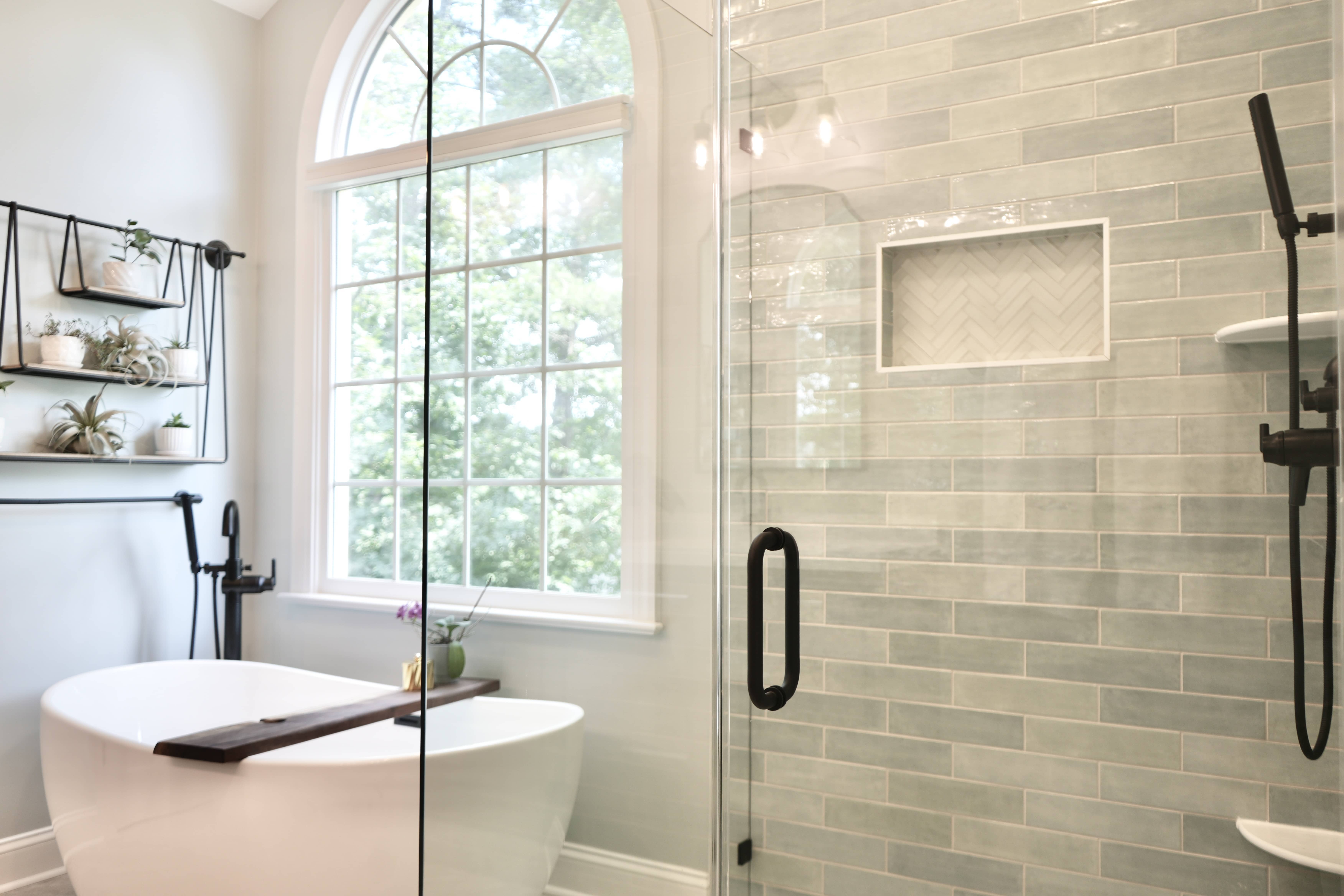 Spa-style bathroom with a freestanding tub beneath an arched window and a green-grey tiled shower