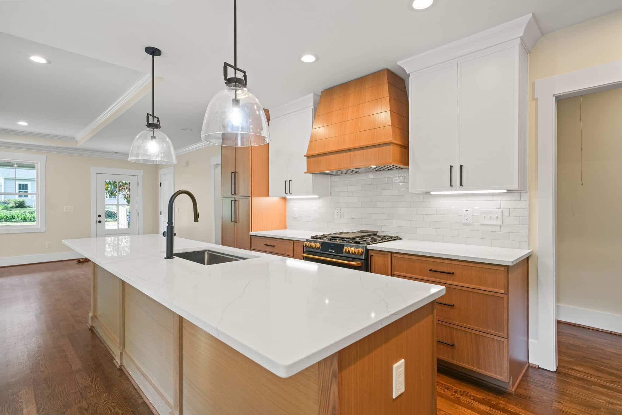 Modern kitchen with a long quartz island, two-tone cabinetry and glass pendant lighting